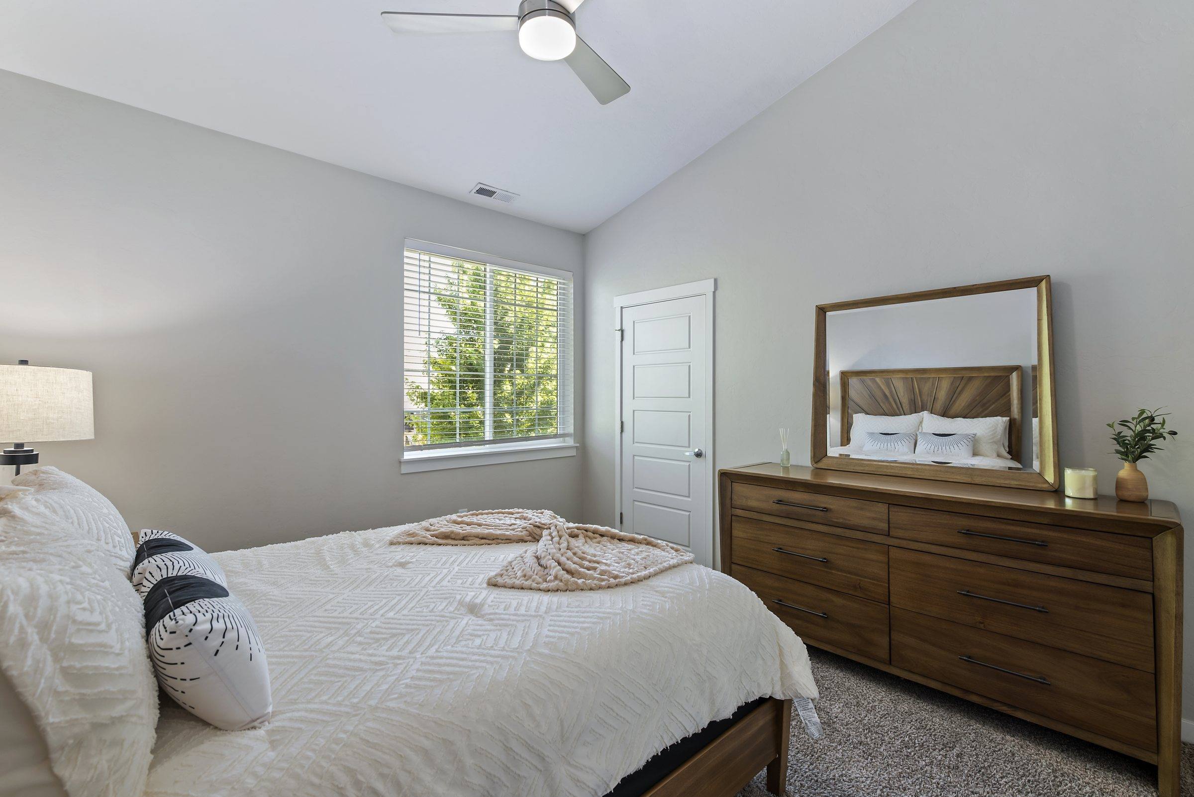 A furnished bedroom with a bed, dresser, and natural light in a model townhome